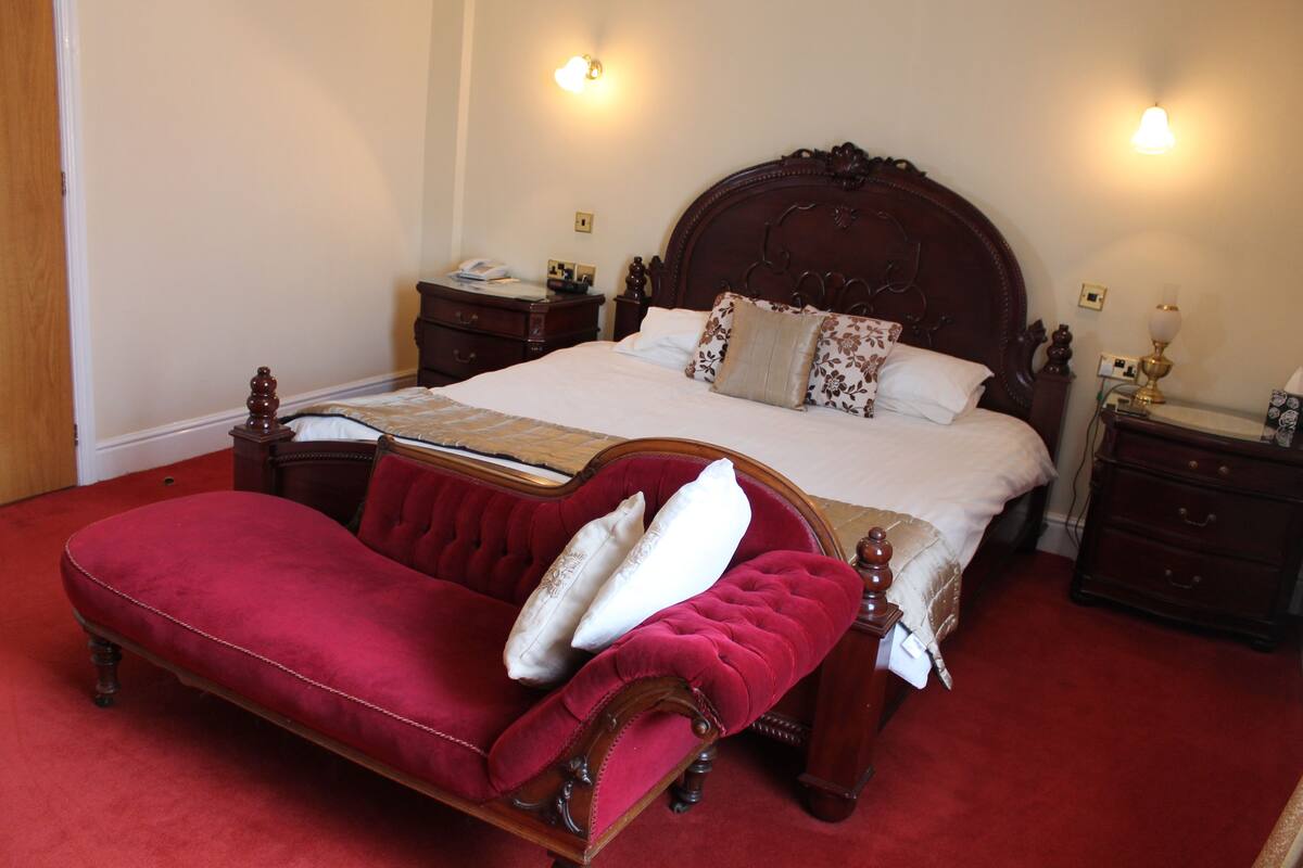 A bedroom with a large bed, a red upholstered bench, and two bedside tables with lamps.