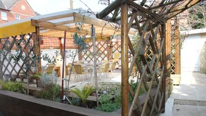 A covered outdoor seating area with chairs and tables, surrounded by a wooden lattice fence and plants. - Longview Hotel (Knutsford)
