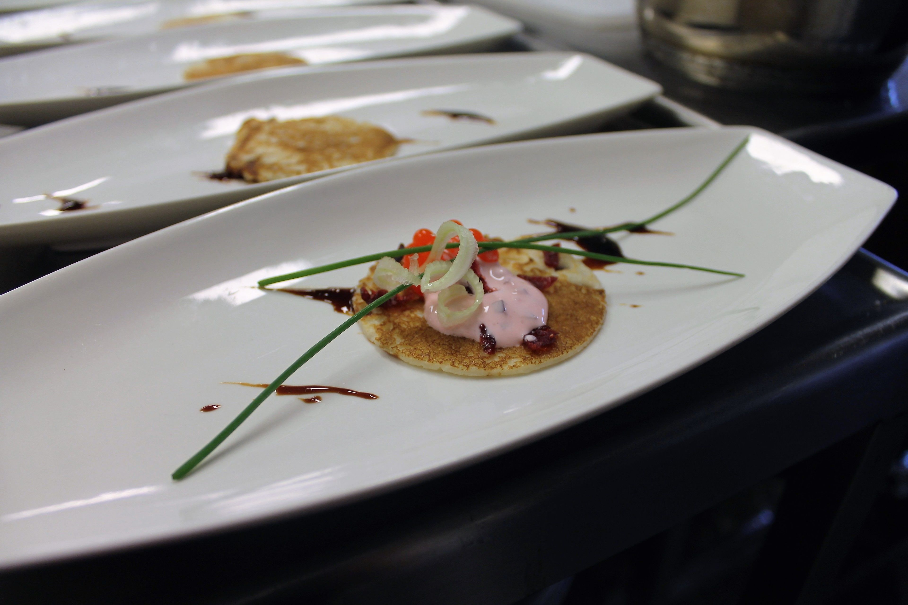 A white plate with a dessert, garnished with green chives and red pepper flakes.