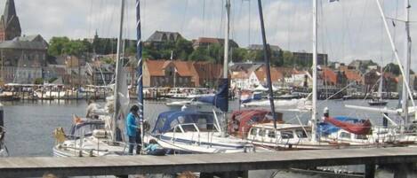 A marina with boats docked, a church in the background, and people sitting by the water.