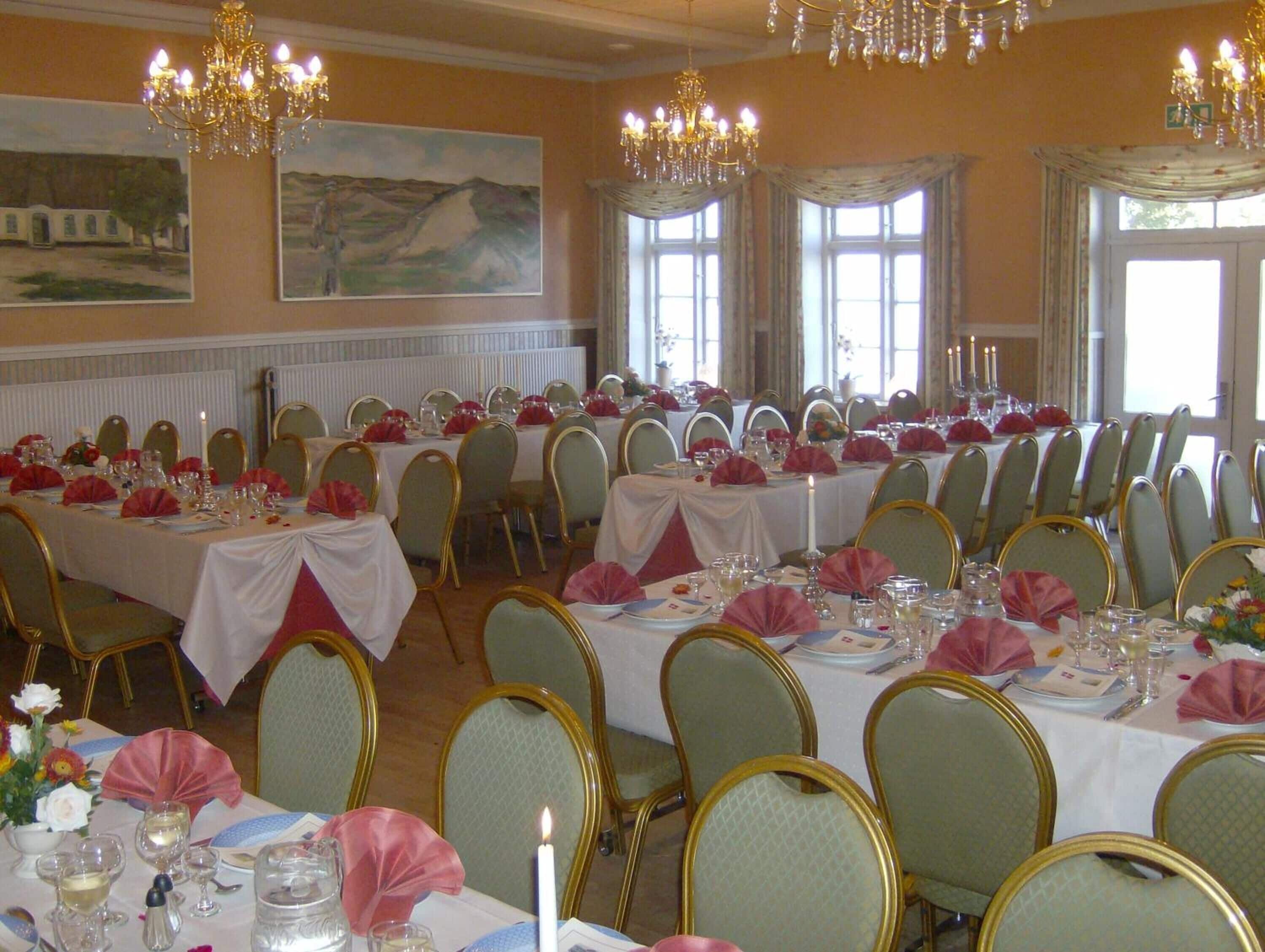 A banquet hall with long tables set for dining, chandeliers, and large windows.