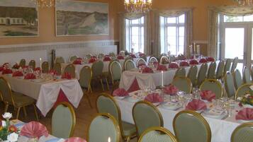 A banquet hall with long tables set for dining, chandeliers, and large windows.