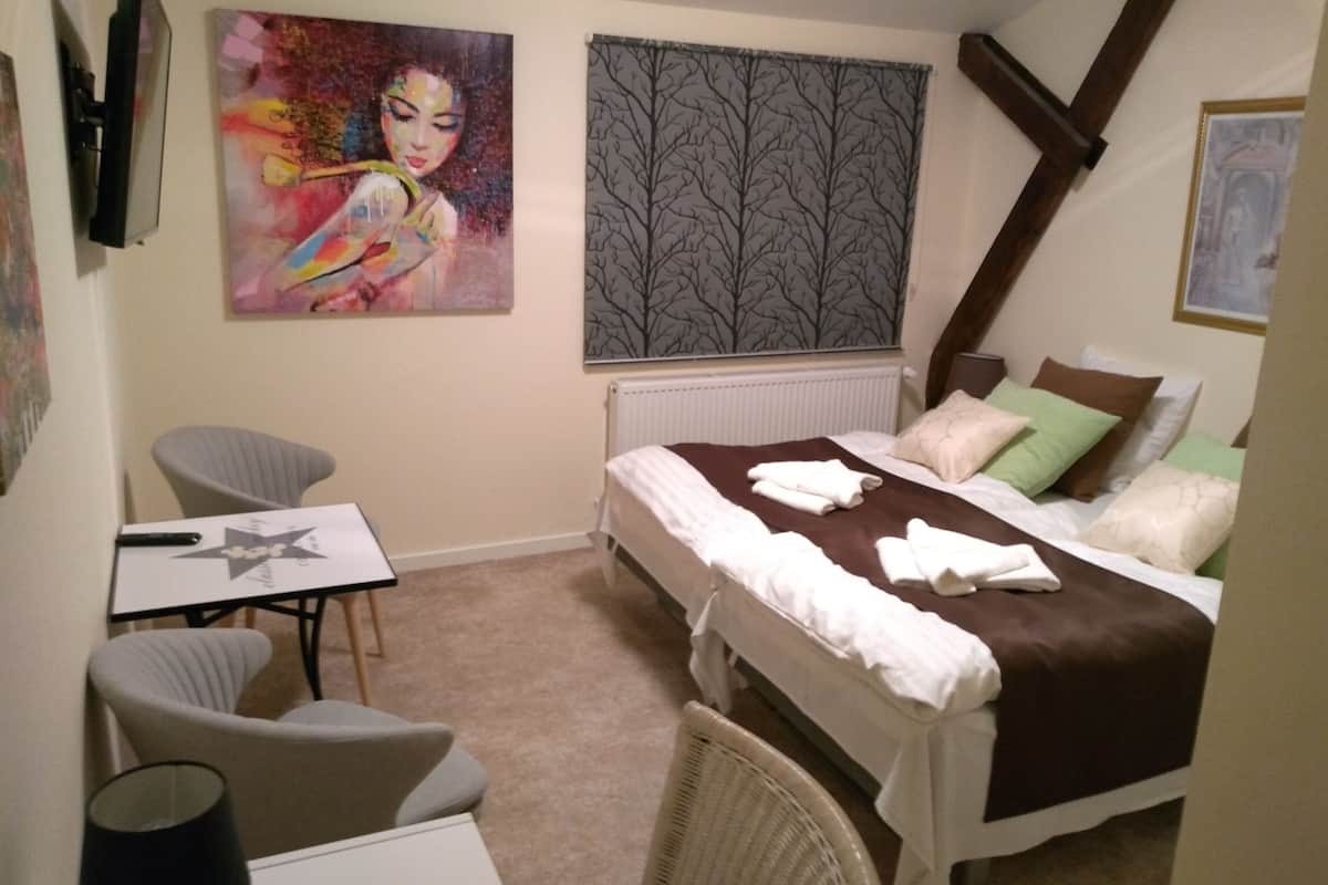 A bedroom with a bed, a chair, a table, and two paintings.