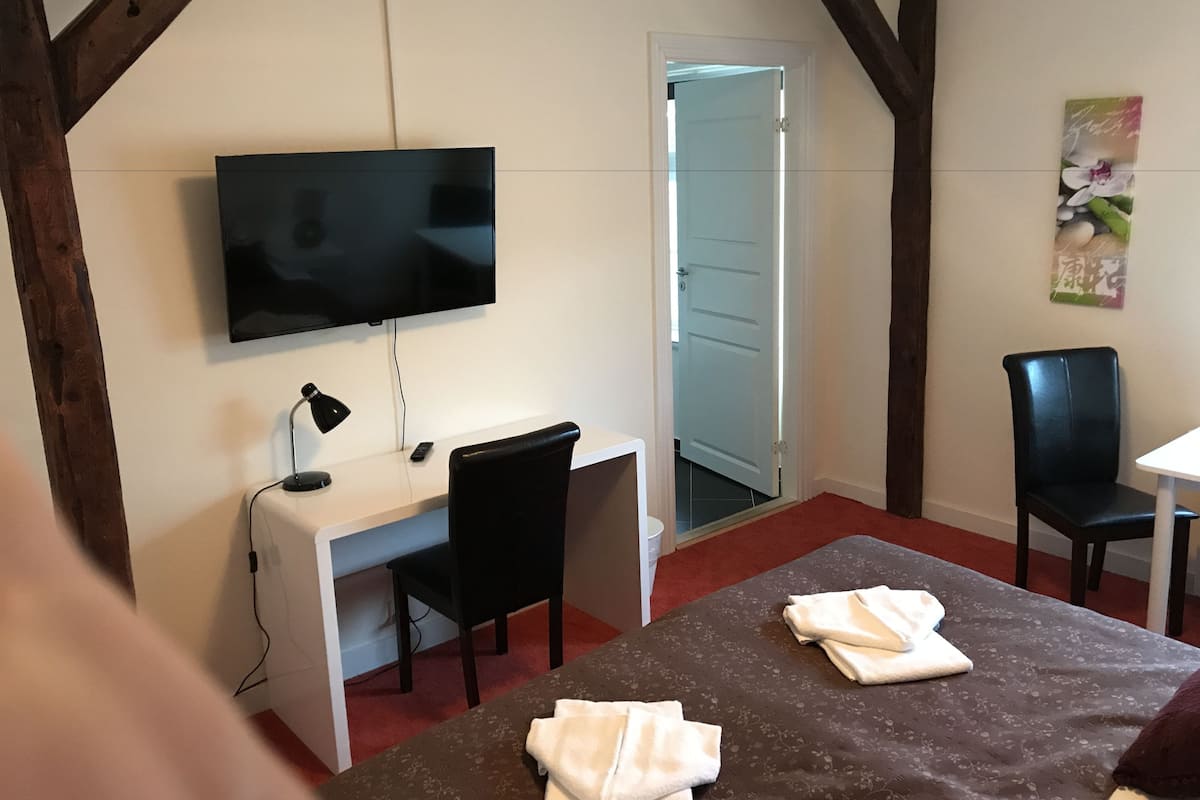 A hotel room with a desk, chair, TV, and a bed with towels.