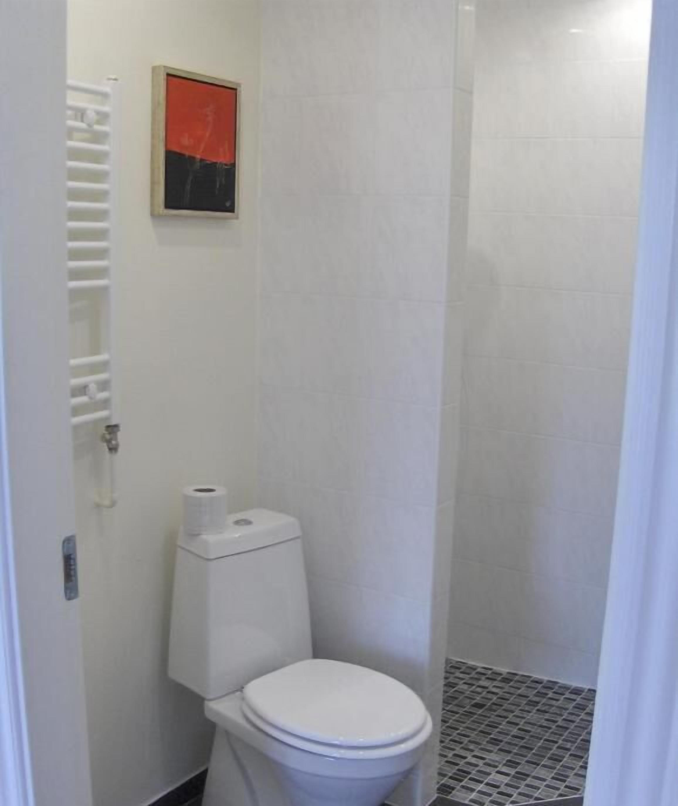 A small, white bathroom with a toilet, a roll of toilet paper, and a shower stall.