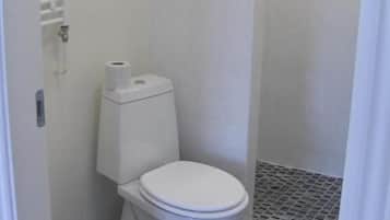 A small, white bathroom with a toilet, a roll of toilet paper, and a shower stall.