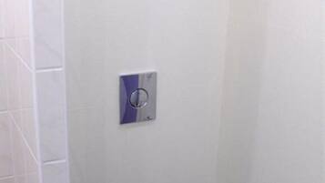 Une salle de bain avec un mur recouvert de carreaux blancs, des toilettes avec un abattant noir, un sèche-mains et une image d’un autobus à deux étages rouge.