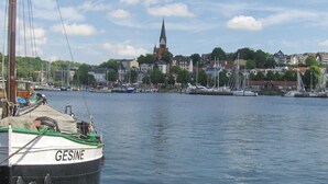 A harbor with boats docked, a church in the background, and a row of buildings along the water. - Hotel Frøslev Kro (Padborg)