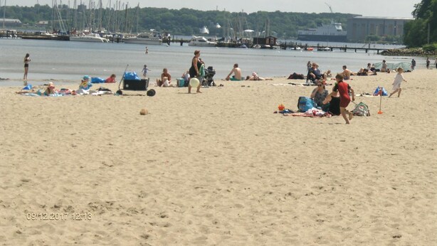 A beach with people sunbathing and playing, boats in the background, and a clear sky. - Hotel Frøslev Kro (Padborg)