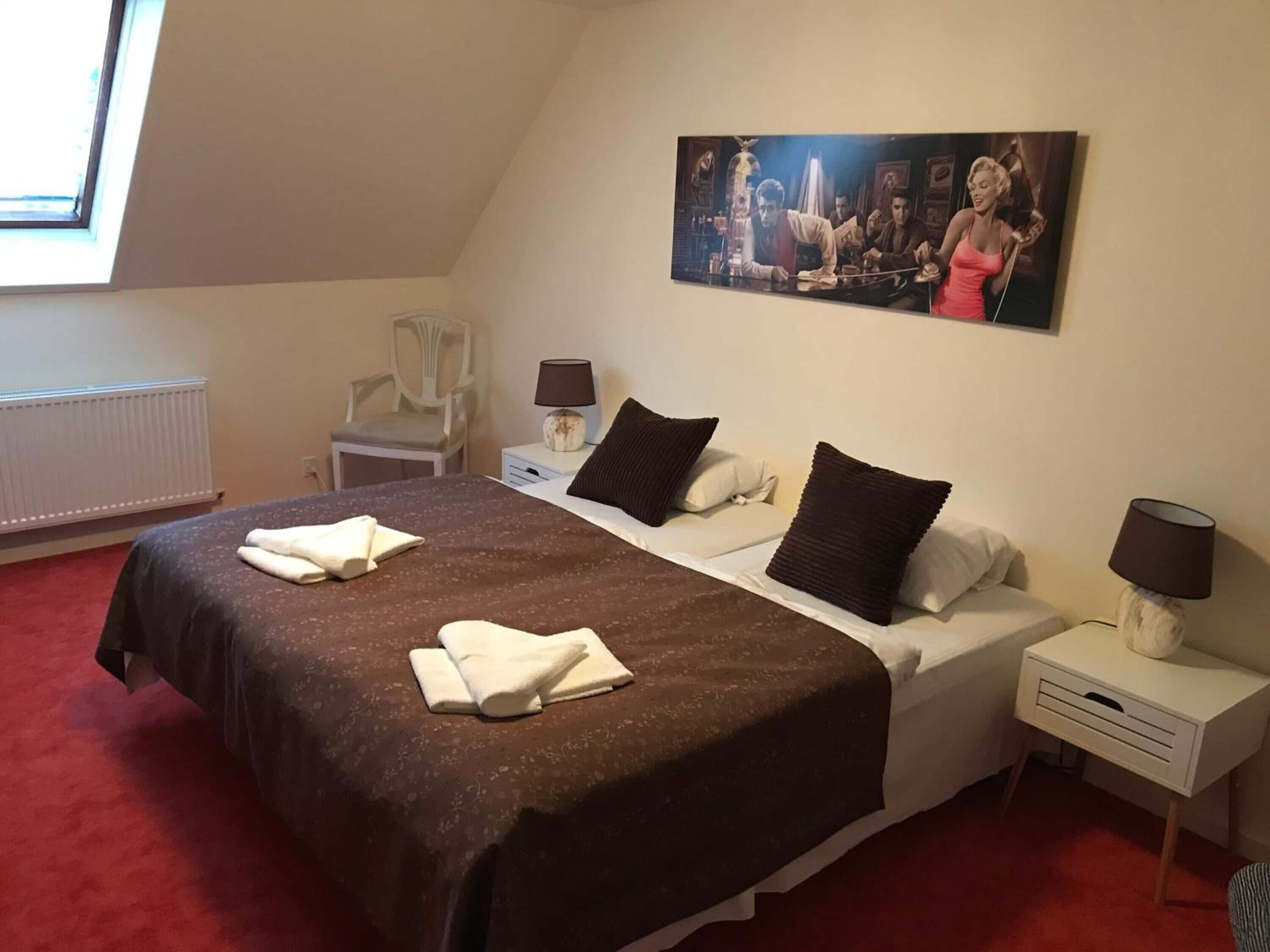 Et hotelværelse med en seng, en stol, et natbord, en lampe og et billede på væggen.
