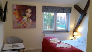 A hotel room with a bed, a chair, a table, a painting, a window, and a radiator. - Hotel Frøslev Kro (Padborg)