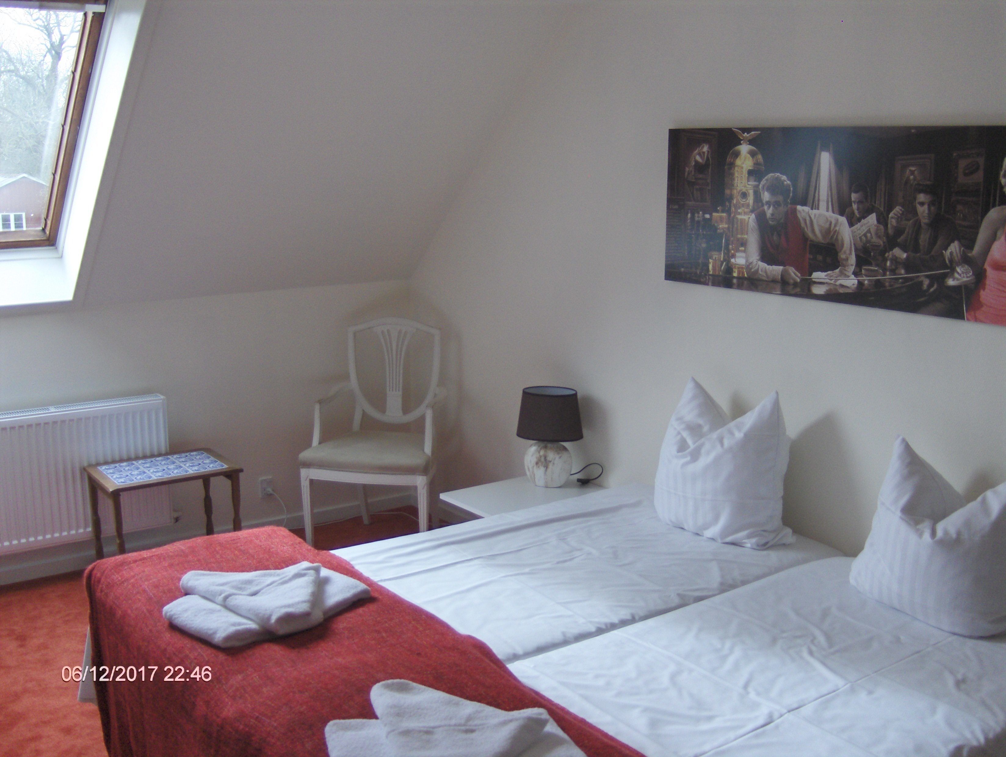 A bedroom with a bed, a chair, a table, a lamp, and a painting on the wall.
