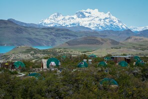 A series of dome-shaped tents in a natural setting with a mountain range and a lake in the background.