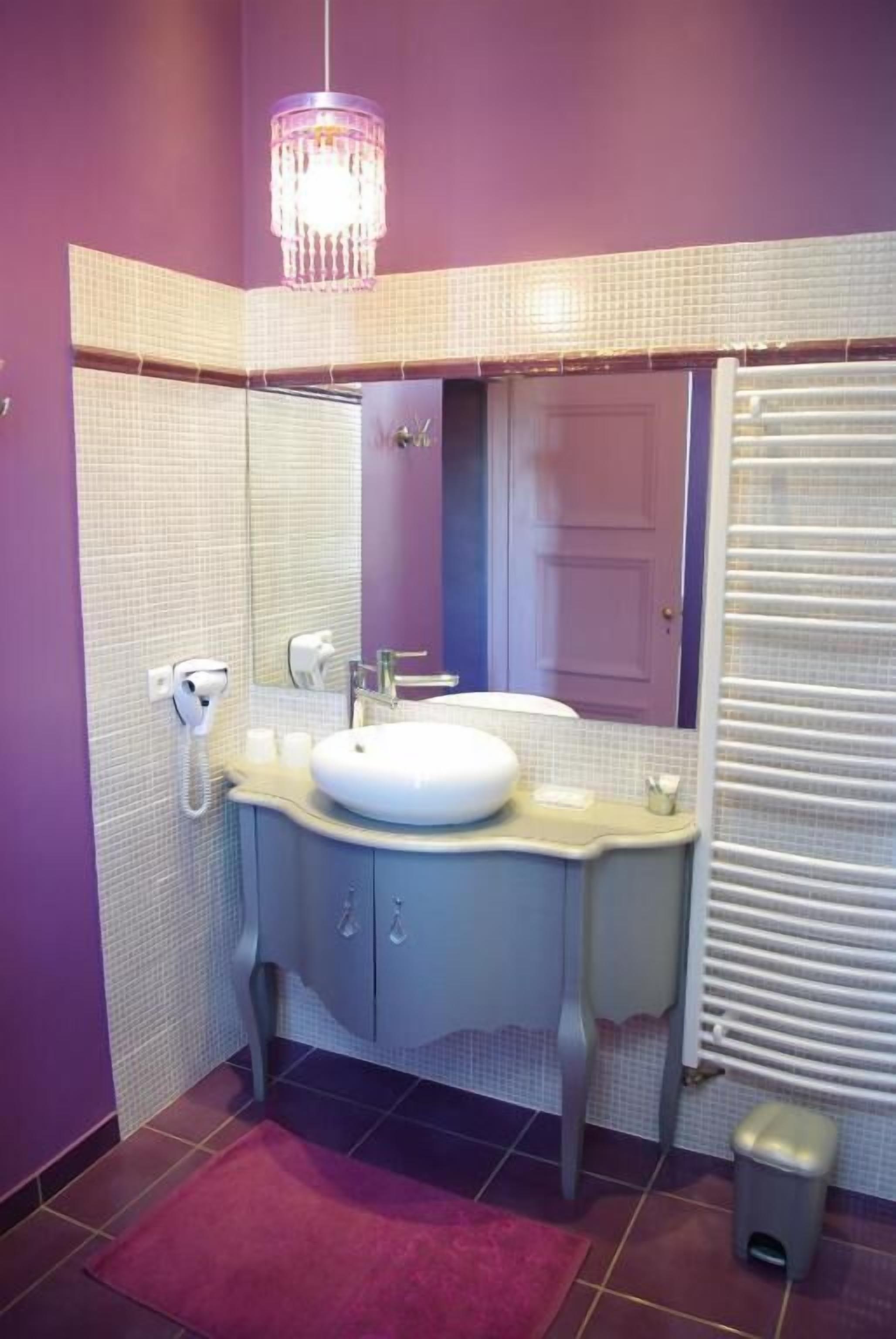 Un baño con un lavabo, tocador y espejo. Hay una araña de cristal sobre el lavabo y una puerta con ventanal.