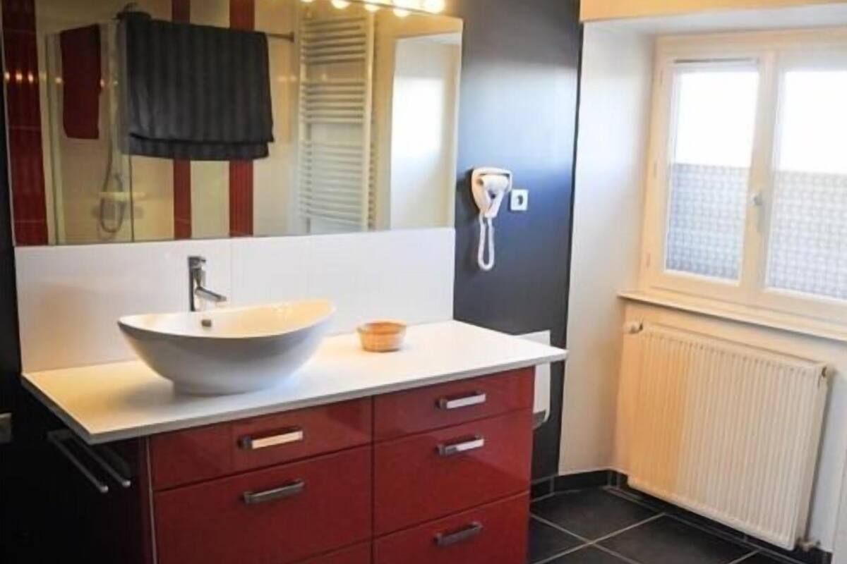 Ein modernes Badezimmer mit einem weißen Waschbecken, roten Schubladen, einem Spiegel und einem Fenster mit Jalousien.