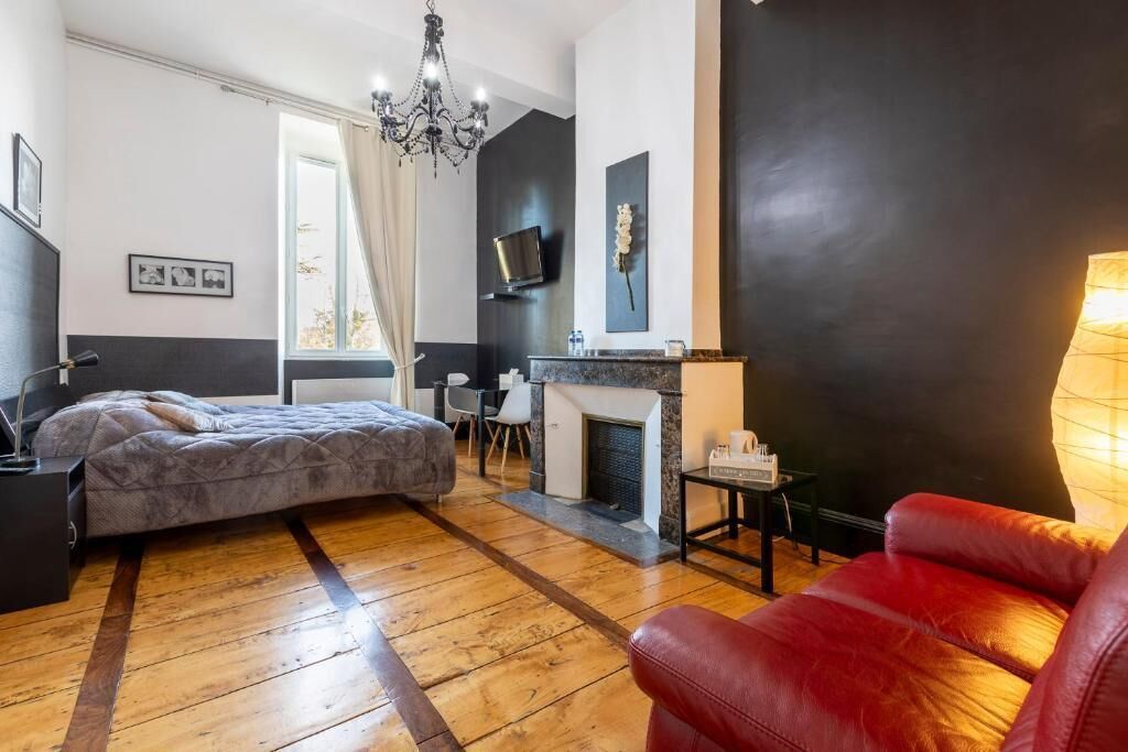 Un dormitorio moderno con cama, un sillón de cuero rojo, chimenea y televisión montada en la pared.