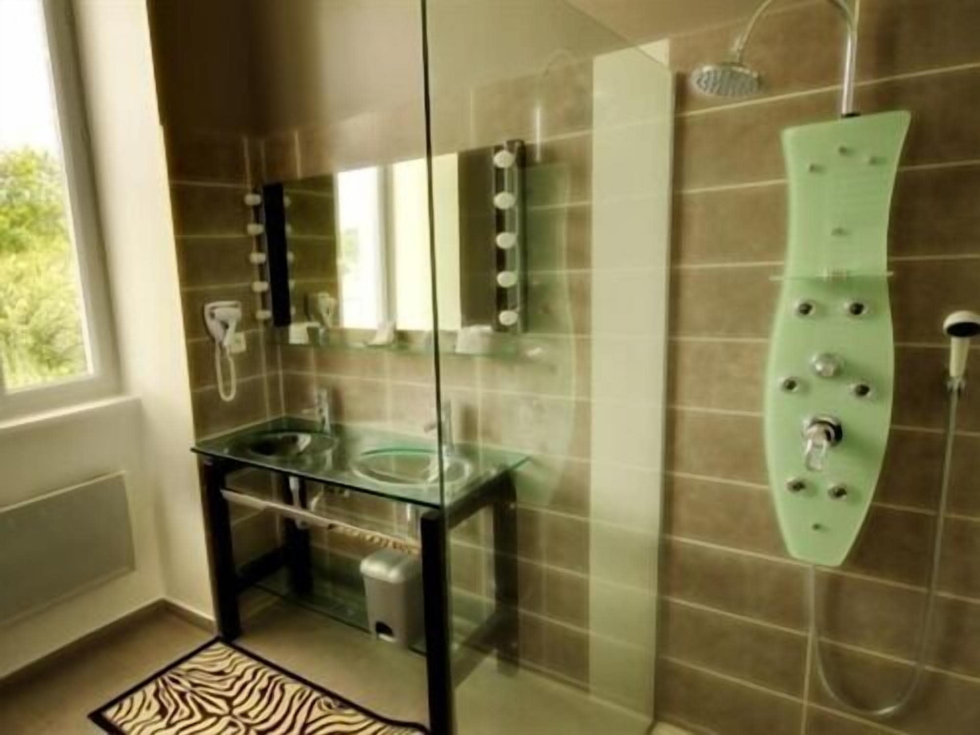 Un baño moderno con cabina de ducha de vidrio, lavamanos de vidrio y alfombra con estampado de cebra.