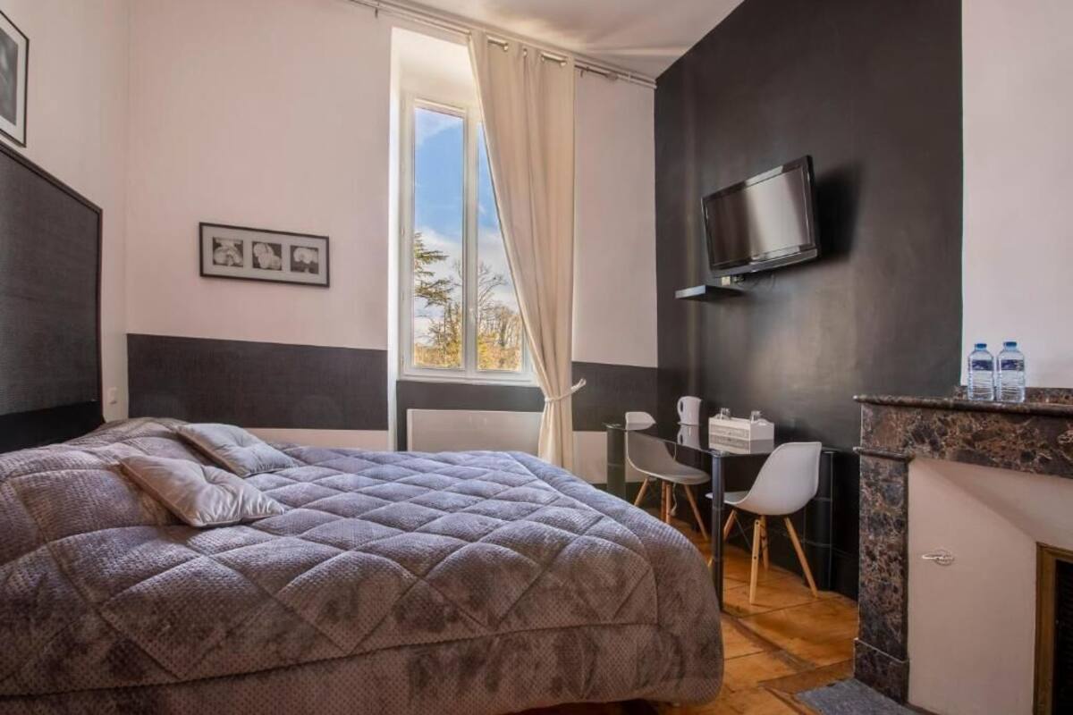Ein Schlafzimmer mit einem großen Bett, einem Schreibtisch, einem Stuhl, einem Fernseher und einem Fenster mit Vorhängen.