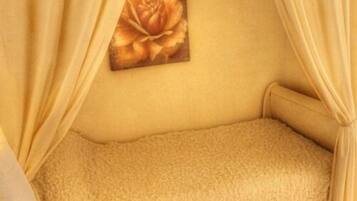 Una habitación con una cama de textura color beige, un cuadro de una rosa en la pared y cortinas amarillas.