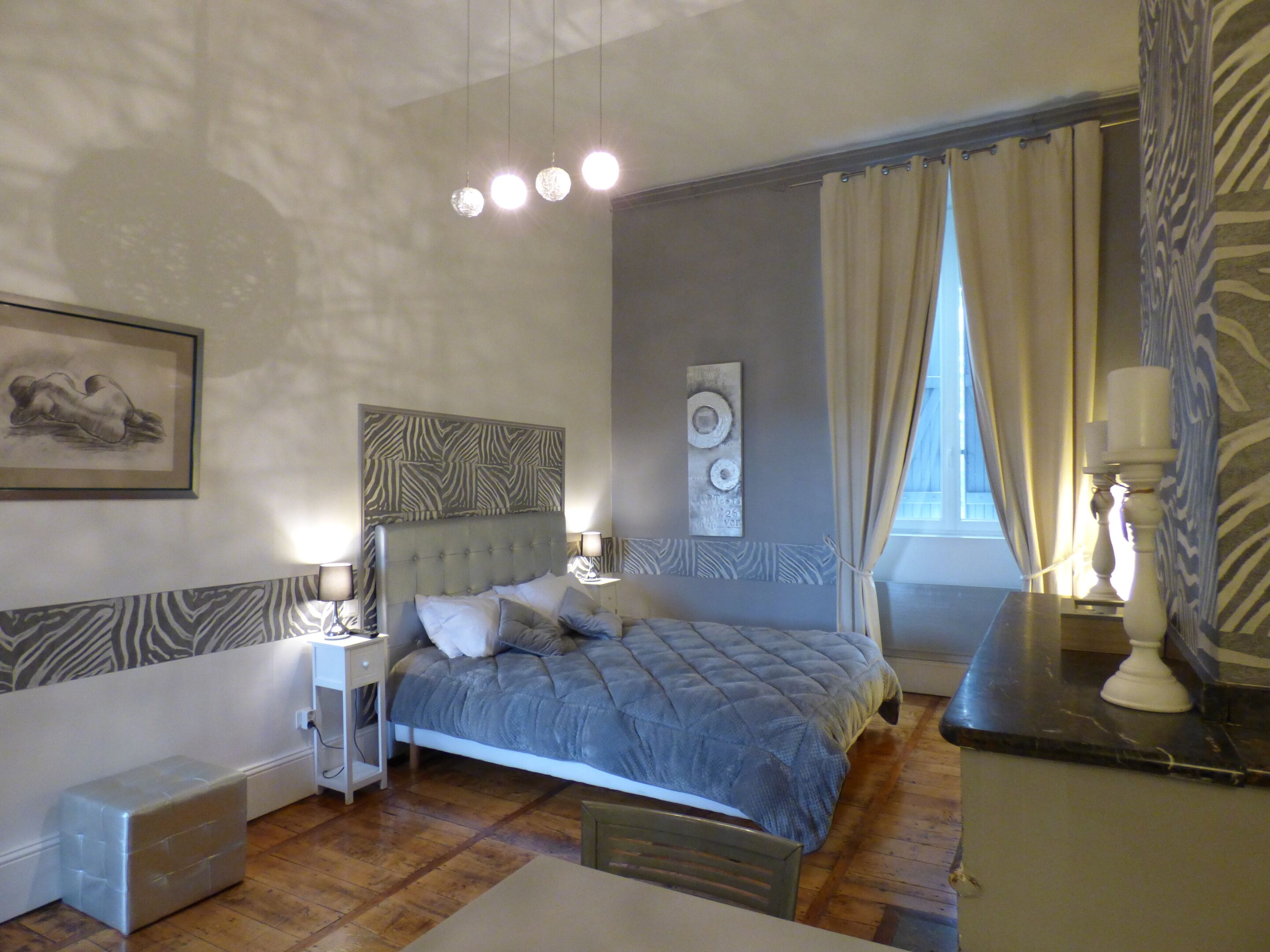 A bedroom with a bed, bedside tables, a nightstand, a dresser, and a window with curtains.