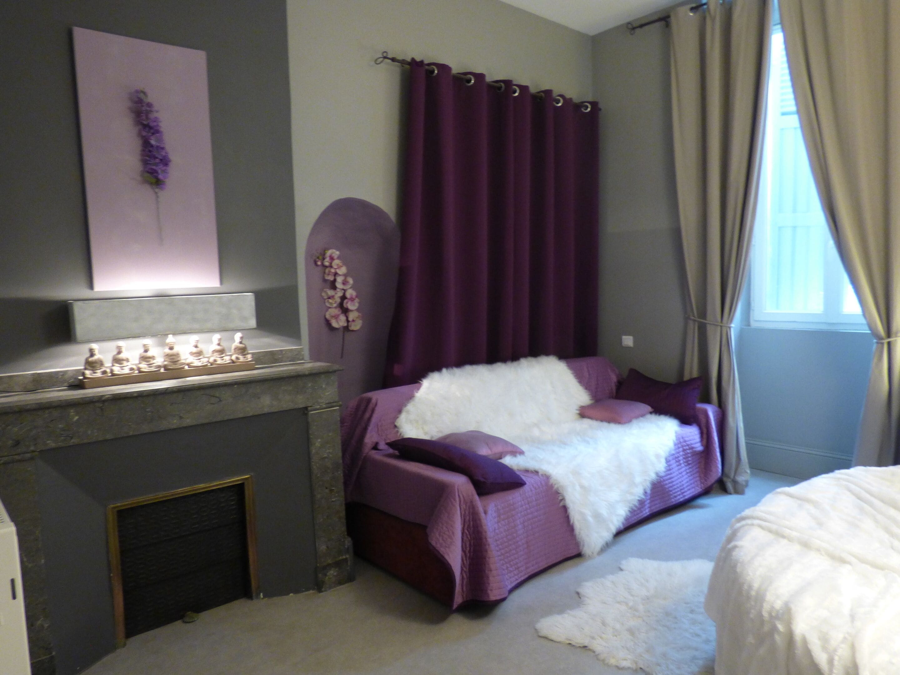 A bedroom with a bed, a fireplace, and purple curtains.