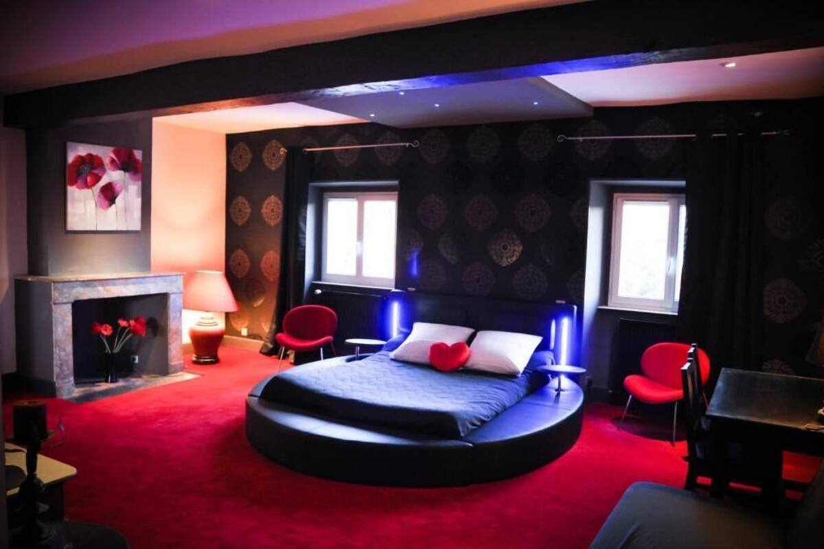 Ein rundes Bett mit einem roten Herz-Kissen, ein Kamin und zwei rote Sessel.
