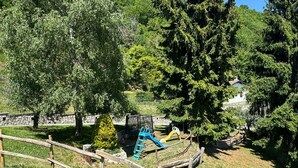 A fenced outdoor area with a playground, trees, and a stone wall. - Cà Vecia (Gargnano)
