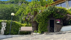 A stone bench, a statue, a tree with ivy, and a building with a wooden facade. - Cà Vecia (Gargnano)