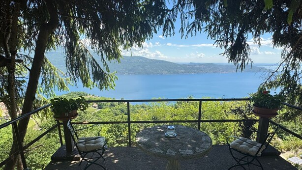 A terrace with a table and chairs, overlooking a body of water and distant hills. - Cà Vecia (Gargnano)