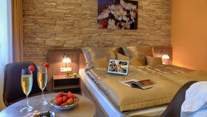 Een hotelkamer met een stenen muur, een bed met een laptop, een tafel met drankjes en snacks, en een bloemenfoto aan de muur.