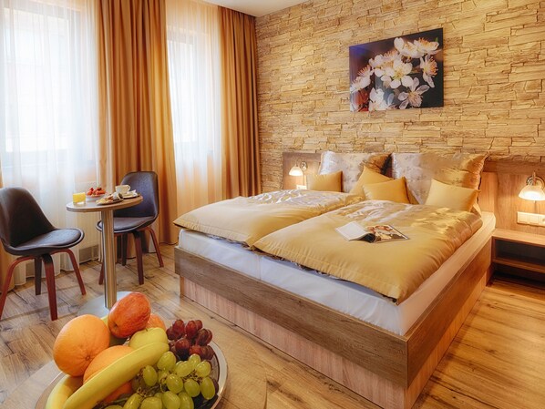 Habitación de hotel con una cama grande, dos mesitas de noche, una pequeña mesa con desayuno y un frutero.