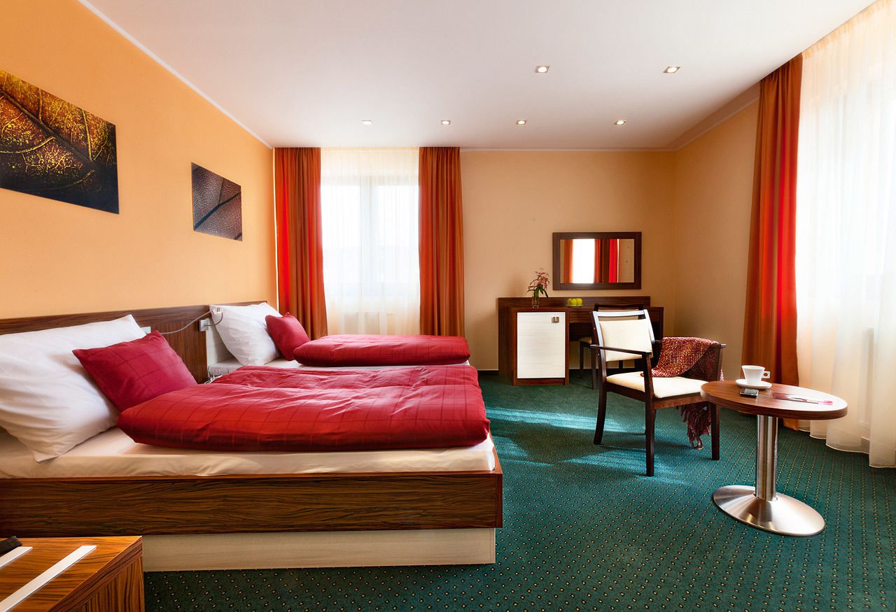 A hotel room with a large bed, a desk, a chair, and a small table.