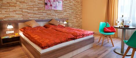 Habitación de hotel moderna con pared de piedra, cama con una manta roja, una mesita con una bebida y una silla.