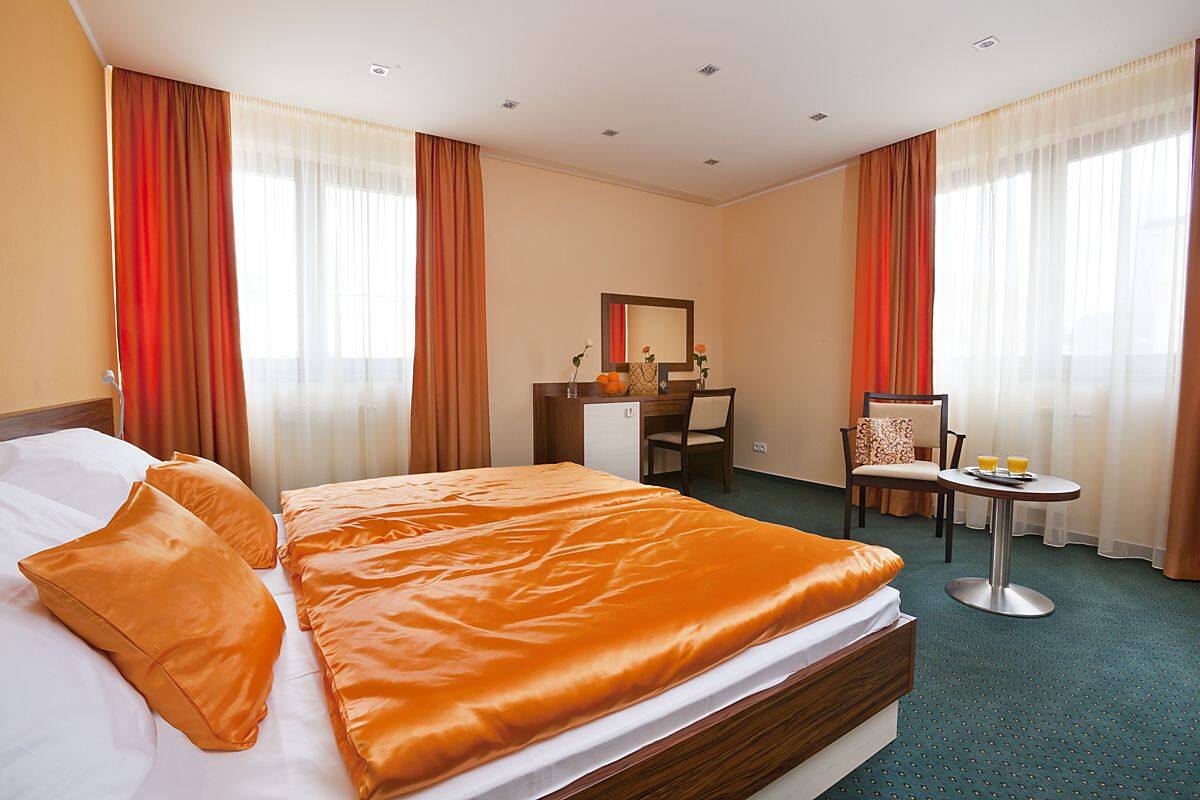 A hotel room with a large bed, a desk, a chair, and a small table with a tray of orange juice.