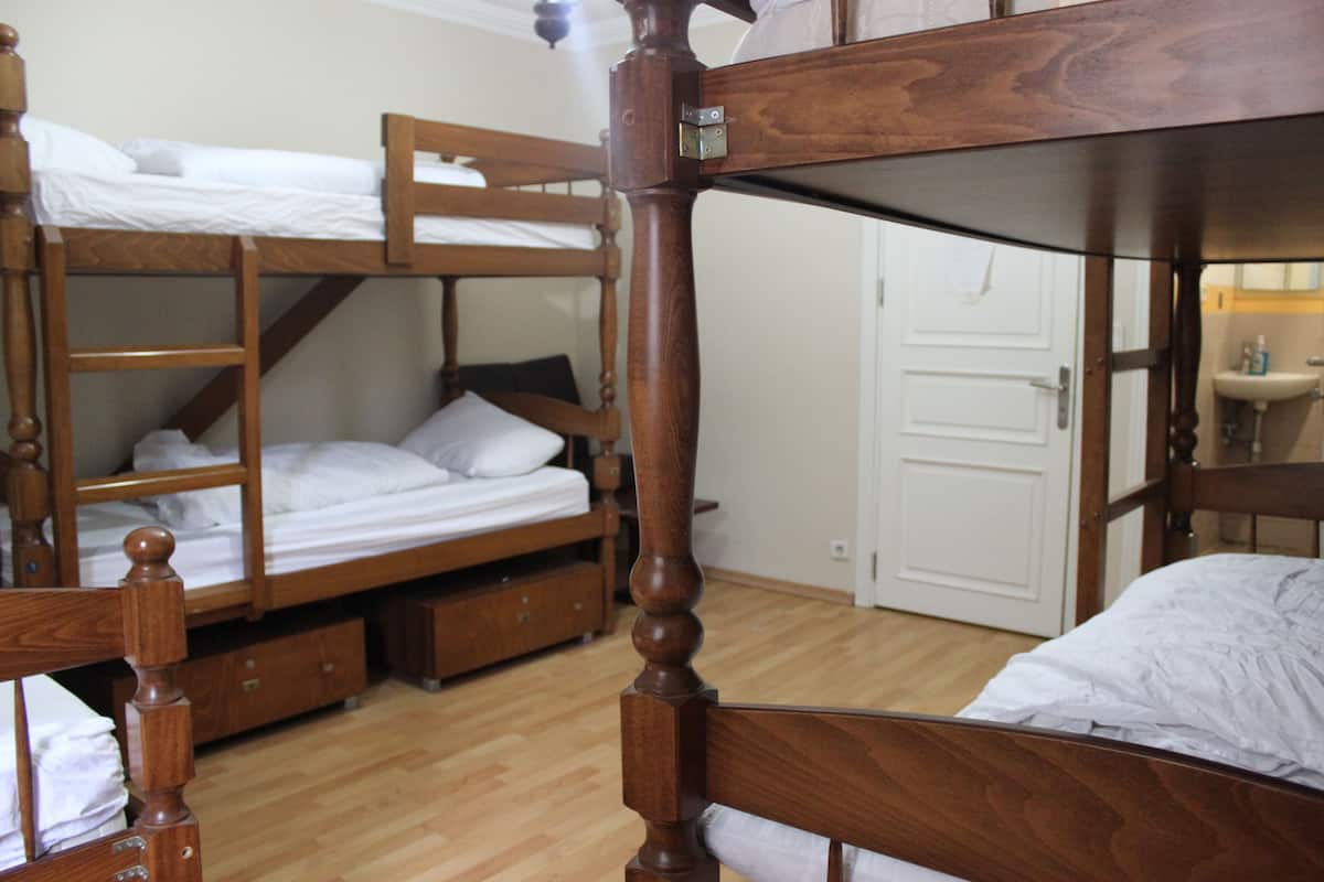 A room with two bunk beds, wooden furniture, a white door, and a small bathroom with a sink.