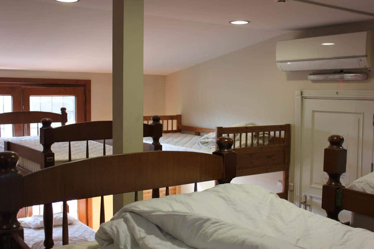 A bedroom with a bunk bed, a single bed, wooden headboards, and an air conditioning unit.