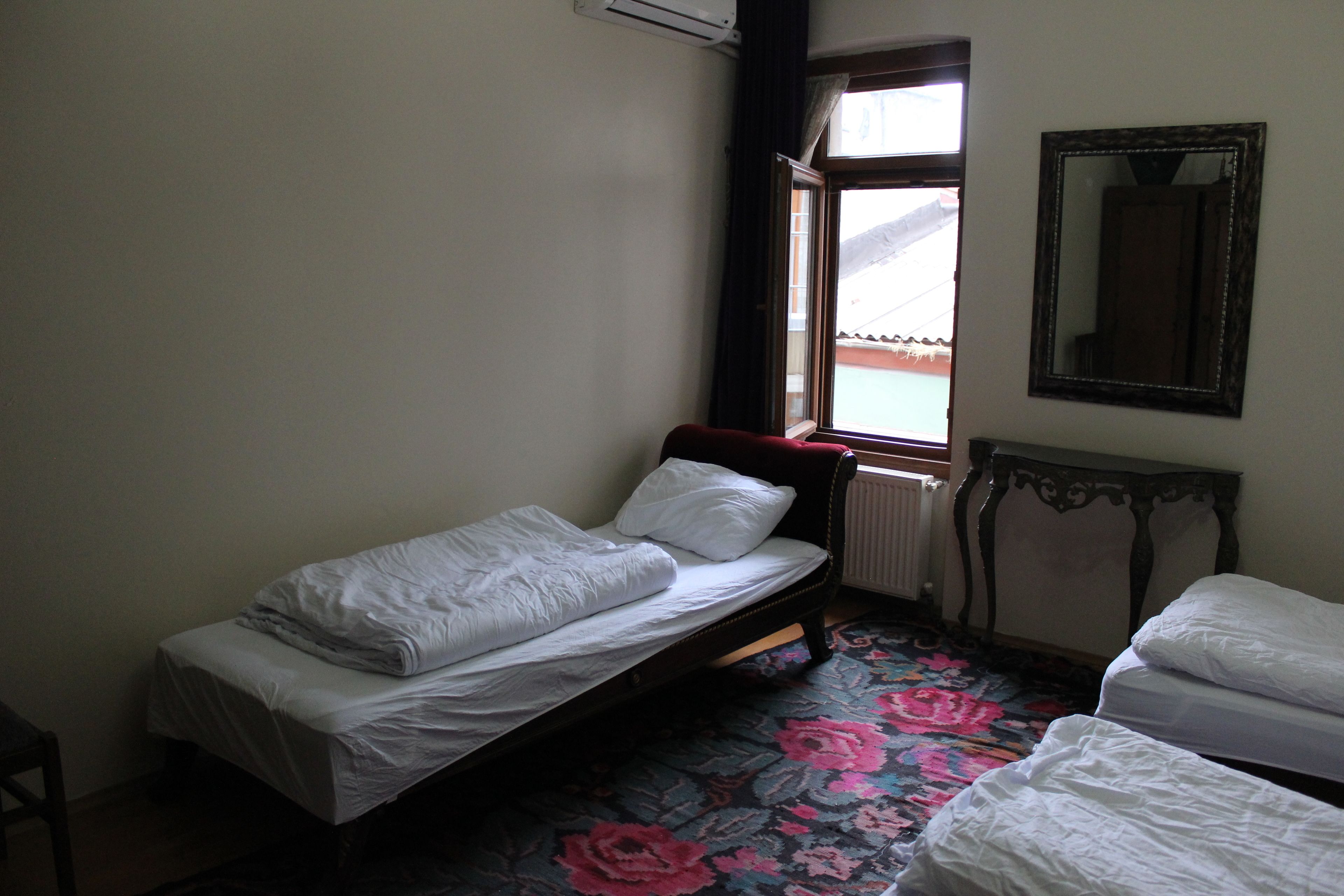 A small bedroom with a single bed, a window, a radiator, and a mirror on the wall.