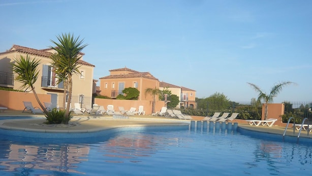 Una piscina con lettini e palme, circondata da edifici con balconi.