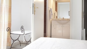 Una camera da letto con un letto, un comodino, una sedia e un bagno con lavandino e specchio.