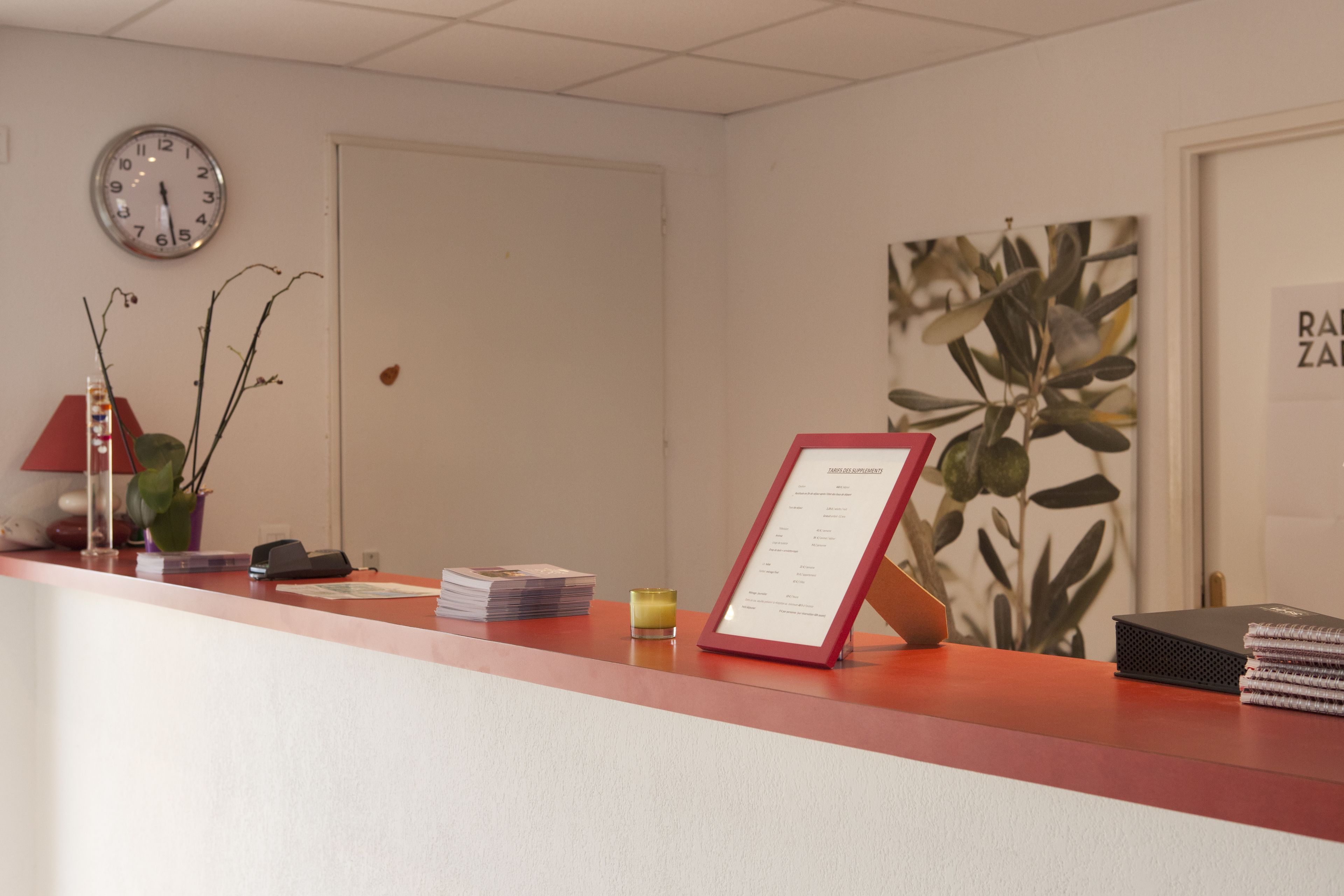 A reception desk with a clock, a framed menu, and a plant.