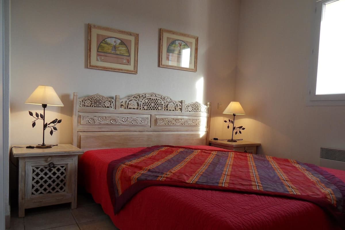 A bedroom with a bed, two bedside lamps, a headboard, and two framed pictures on the wall.