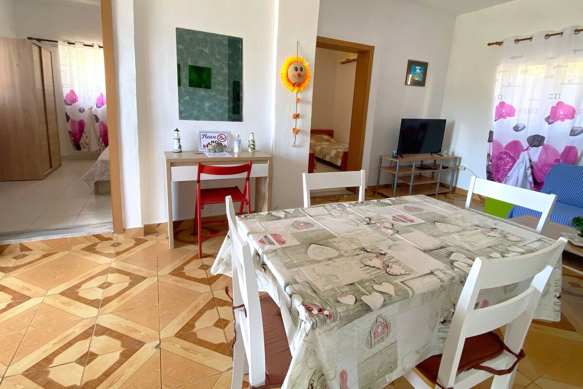A room with a dining table, chairs, a TV, and a bed.