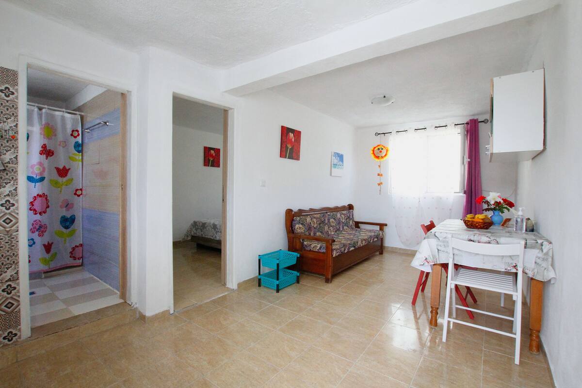 A room with a sofa, a dining table with chairs, a small table with a basket, and a wall-mounted cabinet.