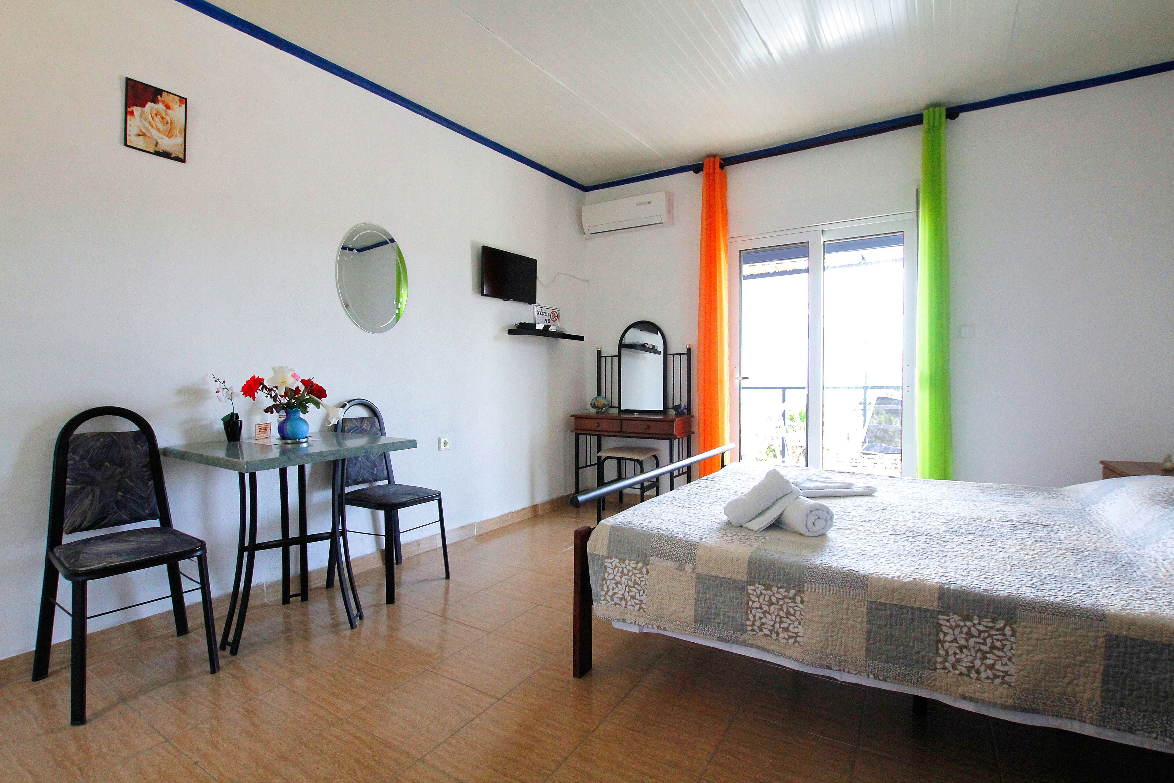 Un dormitorio con cama, escritorio, dos sillas, espejo y ventana con cortinas.
