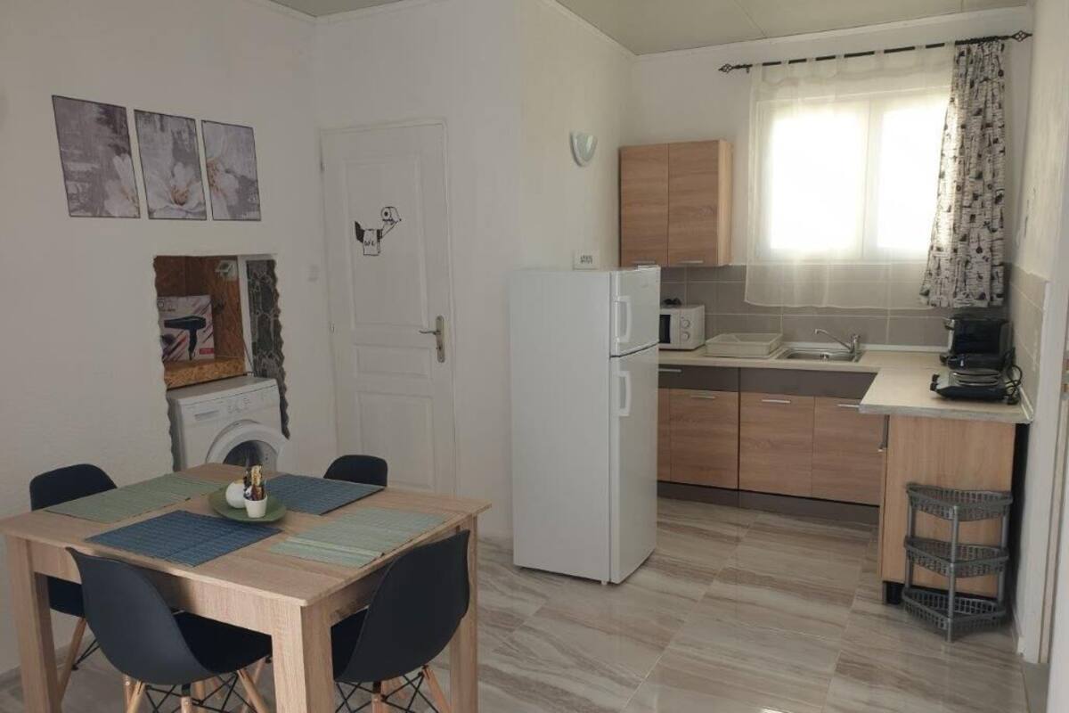 A compact kitchen with a refrigerator, microwave, and sink. There is a dining table with chairs and a small window with curtains.