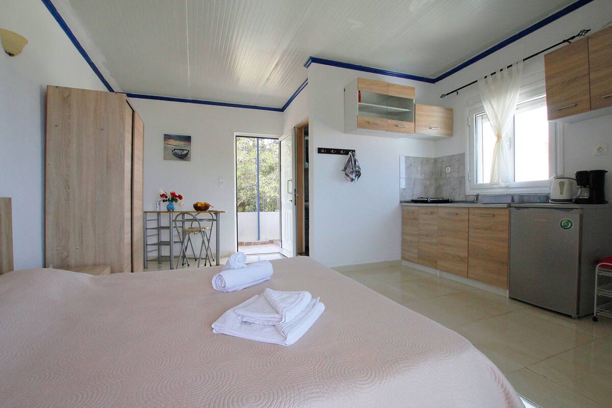 A hotel room with a bed, a small kitchenette, and a bathroom visible through an open door.