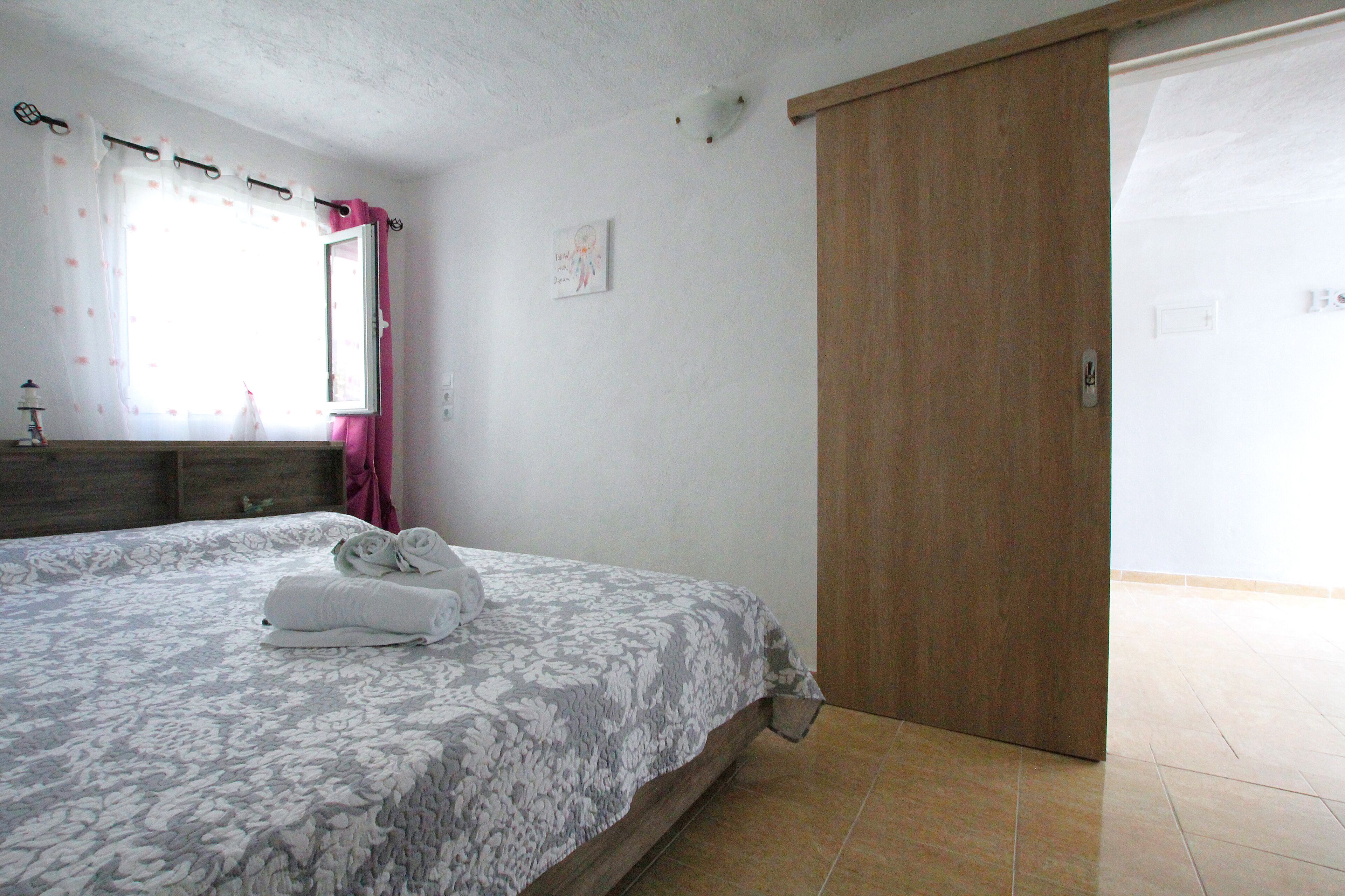 A bedroom with a bed, a wooden wardrobe, a bathroom door, and a window with curtains.