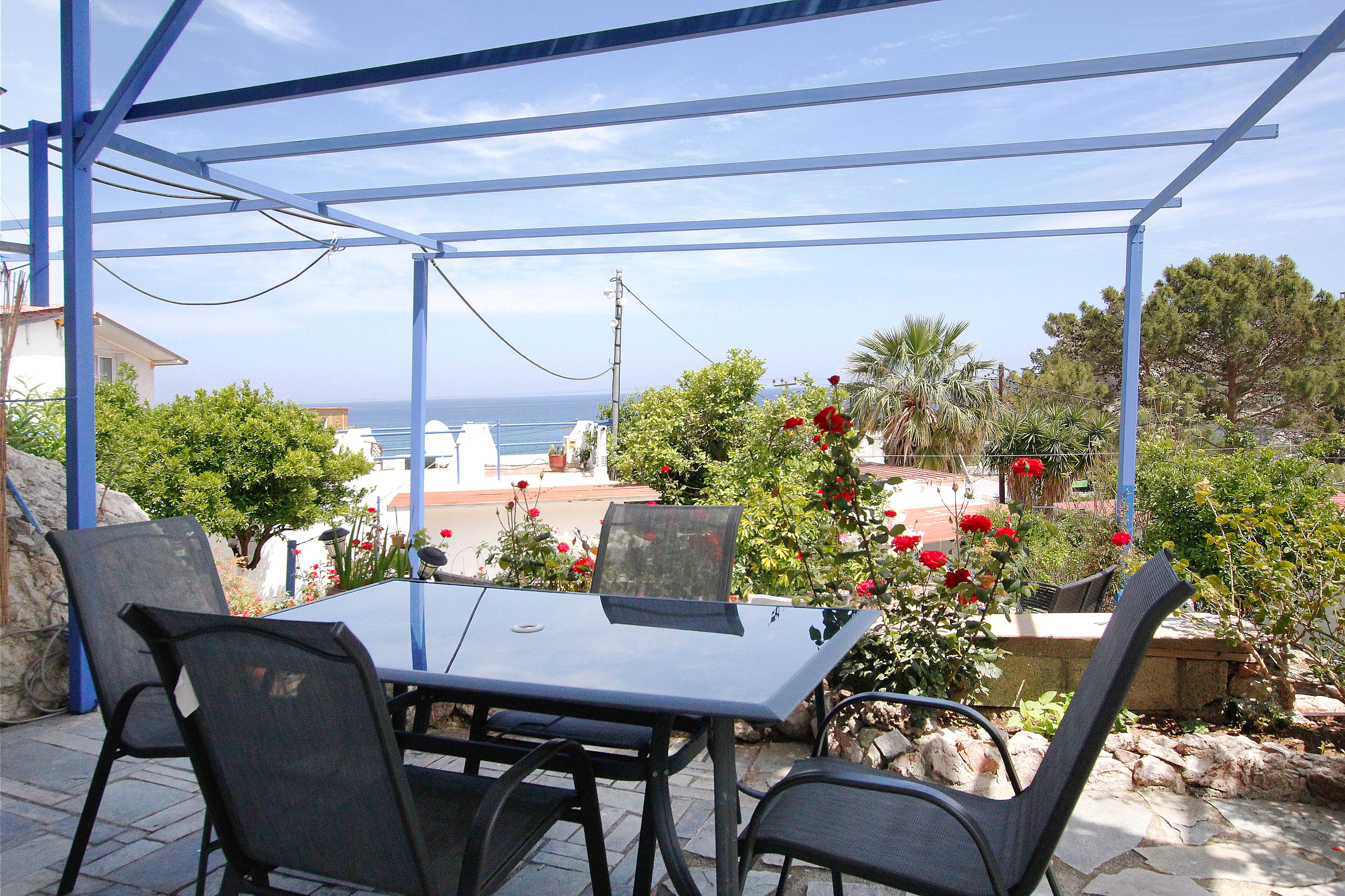 An outdoor patio with a table and chairs, overlooking a coastal area with vegetation and buildings.