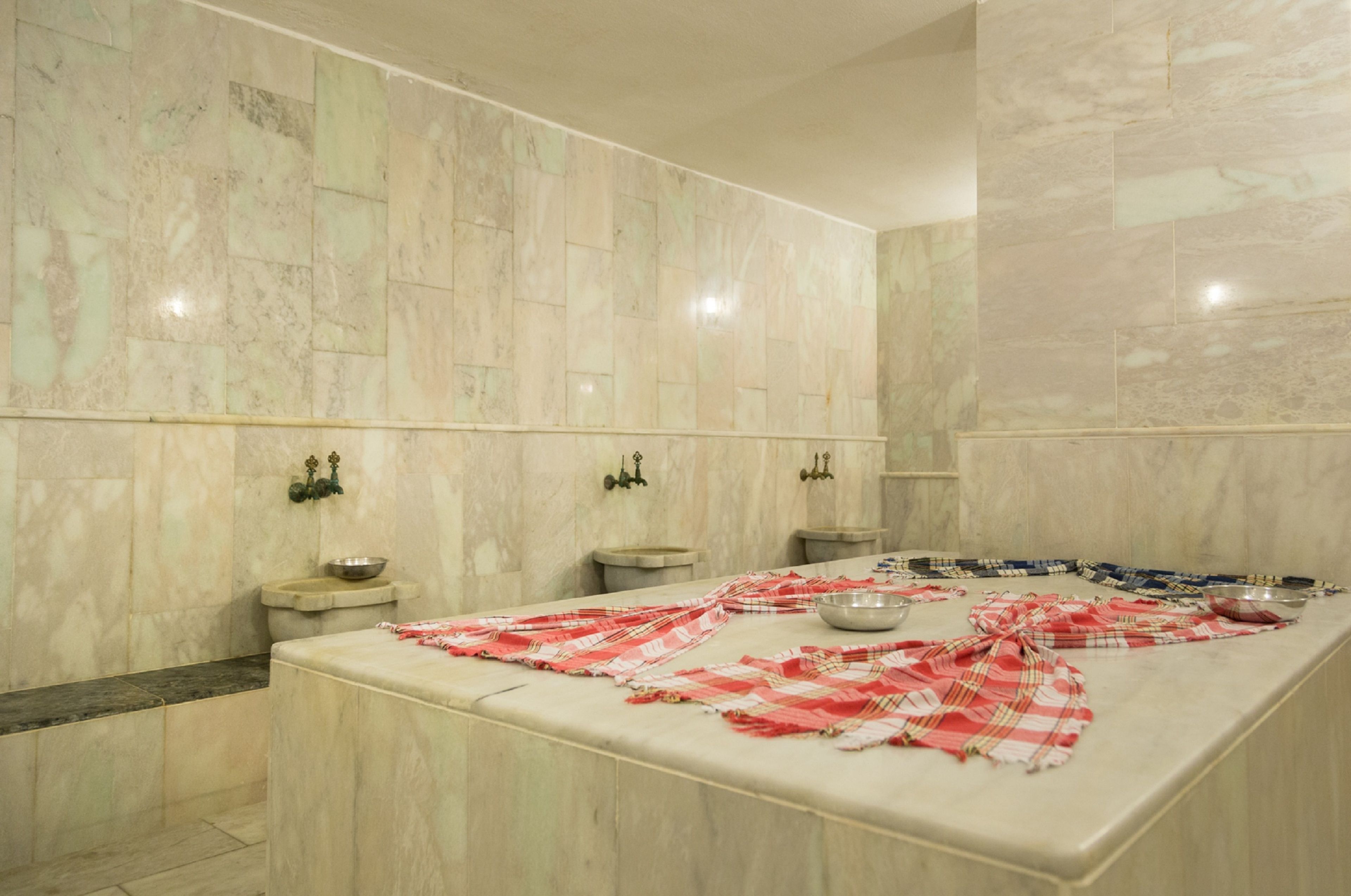 A bathroom with marble walls, multiple sinks, and a table with towels and bowls.