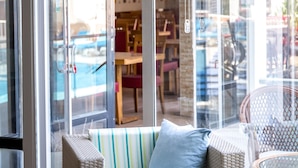 A glass-enclosed outdoor seating area with a cushioned sofa and a glass table, overlooking a pool and a building with a brick facade. - Ponz Boutique Hotel (Kusadasi)
